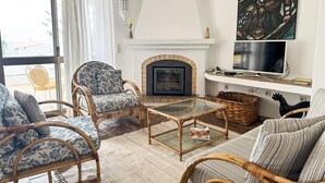 A living room with wicker furniture, a fireplace, a television, and a large window. - Casa ADM 42 - Villa with Pool, Walk to Carvoeiro (Lagoa)