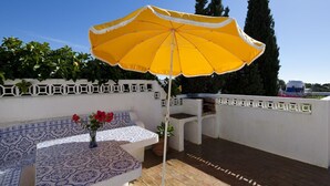 An outdoor patio with a blue and white patterned bench, a yellow umbrella, and a potted plant with red flowers. - Casa ADM 42 - Villa with Pool, Walk to Carvoeiro (Lagoa)