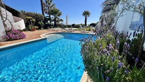 A clear blue pool surrounded by palm trees and lavender plants.