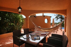 An outdoor patio with wicker furniture, a hammock, and a glass table with books. - Casa Monte Novo, villa with private pool near the beaches and Carvoeiro (Benagil)