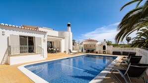 A swimming pool with lounge chairs, a covered patio, and a white building with a tiled roof. - Wonderful holiday villa with airco, heatable pool + jacuzzi on golf development (Carvoeiro)