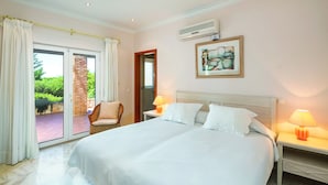 Een hotelkamer met een groot bed, twee bedlampen, een wandairconditioner en een glazen schuifdeur naar een buitenruimte.