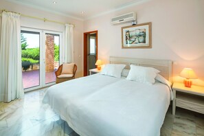 Une chambre d’hôtel dotée d’un grand lit, de deux lampes de chevet, d’un climatiseur mural et d’une porte-fenêtre coulissante donnant sur un espace extérieur.