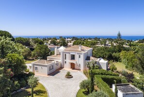 Une villa de style méditerranéen dotée d’une vaste cour, entourée d’une végétation luxuriante et offrant une vue dégagée sur la mer.