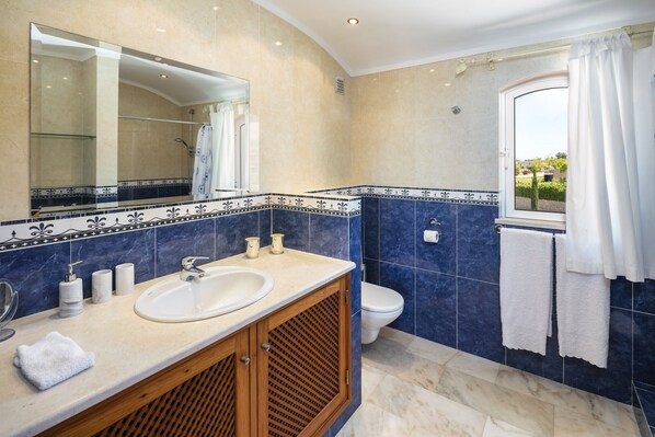 Une salle de bain avec un grand miroir, un lavabo, des toilettes et une fenêtre avec des rideaux.