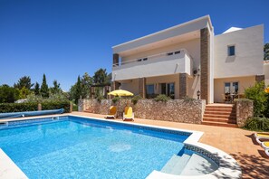 Une maison moderne à deux étages, dotée d’une piscine, de murs en pierre et d’un patio aménagé avec des meubles d’extérieur.