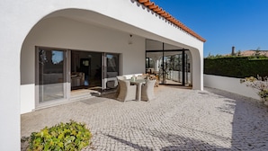 Ein modernes Haus mit Terrasse, ausgestattet mit Tisch und Stühlen, großen Glasürennen, die zu einem Innenbereich führen, und einem Ziegeldach.