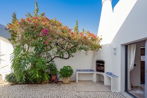 A courtyard with a white wall, a potted plant, a bench, and a small outdoor grill. - Casa Blanca, 3 bedroom villa with air conditioning and private pool (Carvoeiro)
