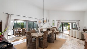 Ein geräumiger Essbereich mit Holztisch und Korbstühlen, einer Chandelierleuchtre und Blick durch große Fenster.