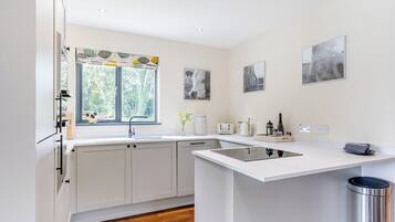 A modern kitchen with a window, white cabinets, a sink, and a trash can.