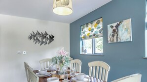 Un comedor con una mesa de madera dispuesta para cuatro, sillas blancas, un florero con flores y obras de arte en las paredes.