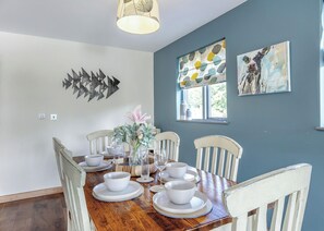 Un comedor con una mesa de madera dispuesta para cuatro, sillas blancas, un florero con flores y obras de arte en las paredes.