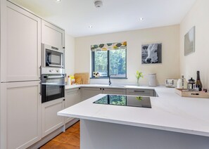 A modern kitchen with a central island, built-in oven, microwave, and a window with a view. - Stunning two storey contemporary lodge on the edge of the lake. (Anglesey)