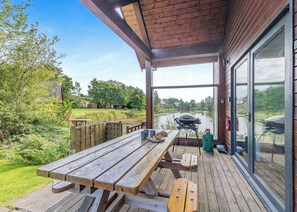 Un'area esterna coperta con un tavolo e panche in legno, un barbecue e vista su un fiume.