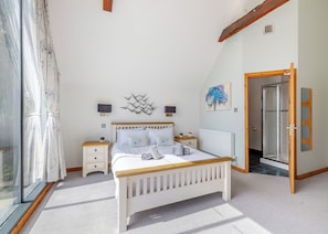 A bedroom with a bed, bedside tables, a radiator, a painting, and a shower area. - Stunning two storey contemporary lodge on the edge of the lake. (Anglesey)