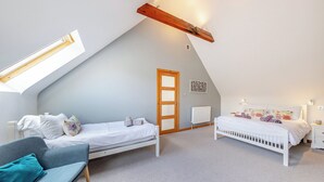 Un dormitorio con techo inclinado, dos camas, una silla, un radiador y una puerta.