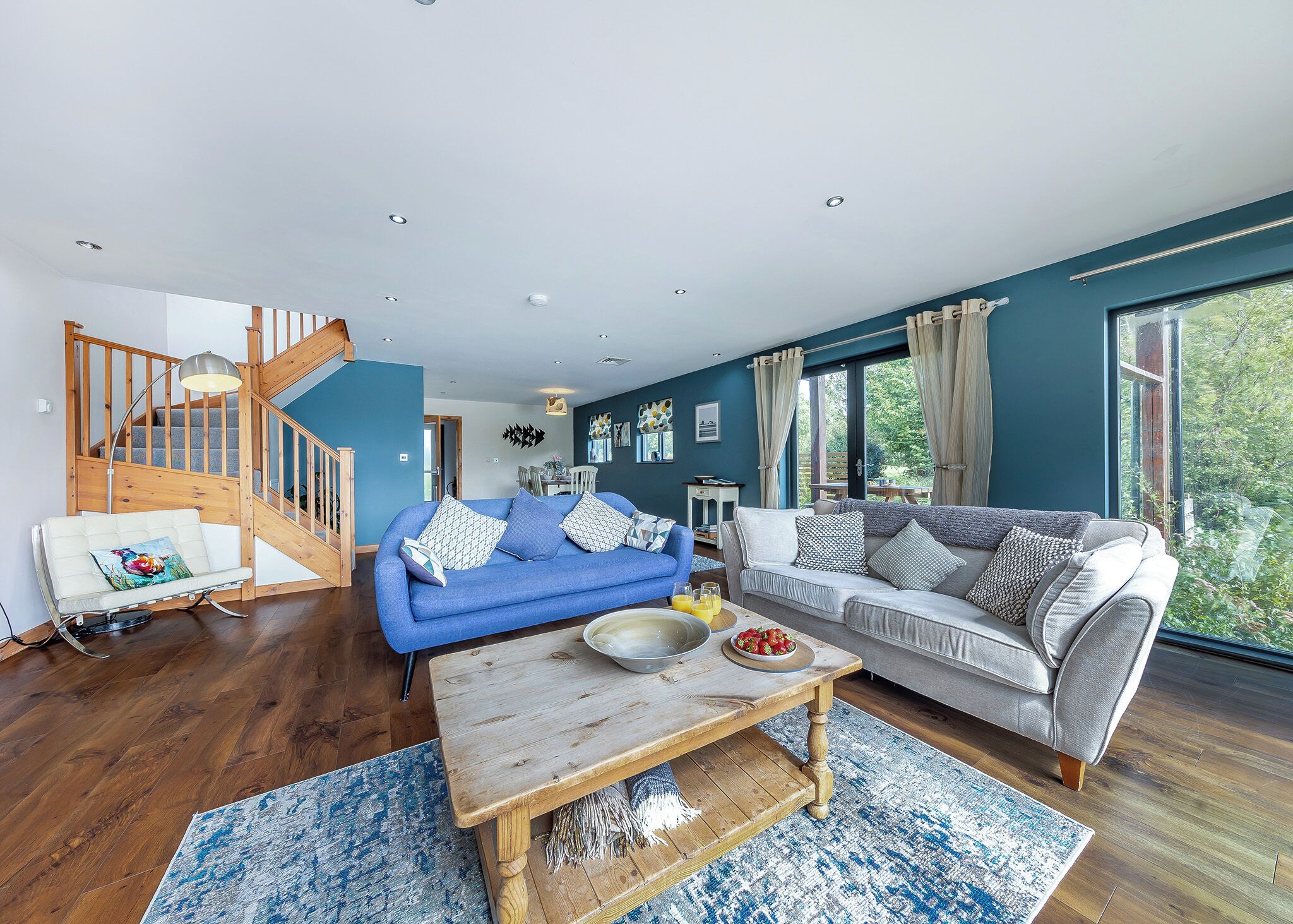 A spacious living room with a blue sofa, a grey sofa, a wooden coffee table, and a staircase.