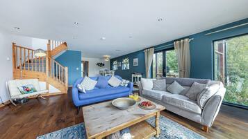 A spacious living room with a blue sofa, a grey sofa, a wooden coffee table, and a staircase.