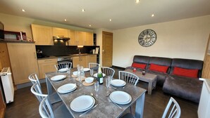 Un espacio habitable compacto con comedor, kitchenette y un sofá con cojines rojos.