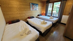 Habitación de cabaña de madera con dos camas, cada una con ropa blanca y toallas, un cuadro en la pared y un ventanal con cortinas.