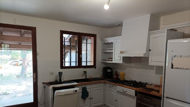 A kitchen with white cabinets, a stove, a refrigerator, and a window with bars. - Country house in the heart of the Landes de Gascogne (Caubeyres)