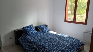 A bedroom with a bed, two pillows, a window, and a radiator. - Country house in the heart of the Landes de Gascogne (Caubeyres)