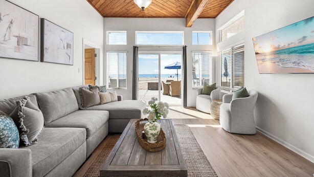 A spacious living room with a wooden ceiling, large windows, and a view of the beach.