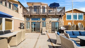 A two-story house with a balcony, outdoor seating area, and surfboards against the wall.