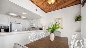 A modern kitchen with white cabinets, a wooden dining table, and a potted plant. - 3 Bedroom Oceanfront Home on 41st St (Newport Beach)
