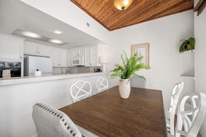A modern kitchen with white cabinets, a wooden dining table, and a potted plant.