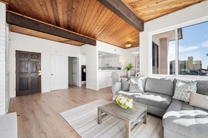 A spacious living area with a wooden ceiling, a gray sofa set, and a view of the city through large windows.