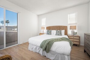 Un dormitorio con una cama grande, una mesita de noche con lámpara, un aparador y un ventanal corredizo que da a un balcón.