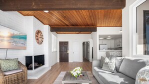 A living room with a fireplace, a sofa, a coffee table with flowers, and a kitchen in the background. - 3 Bedroom Oceanfront Home on 41st St (Newport Beach)