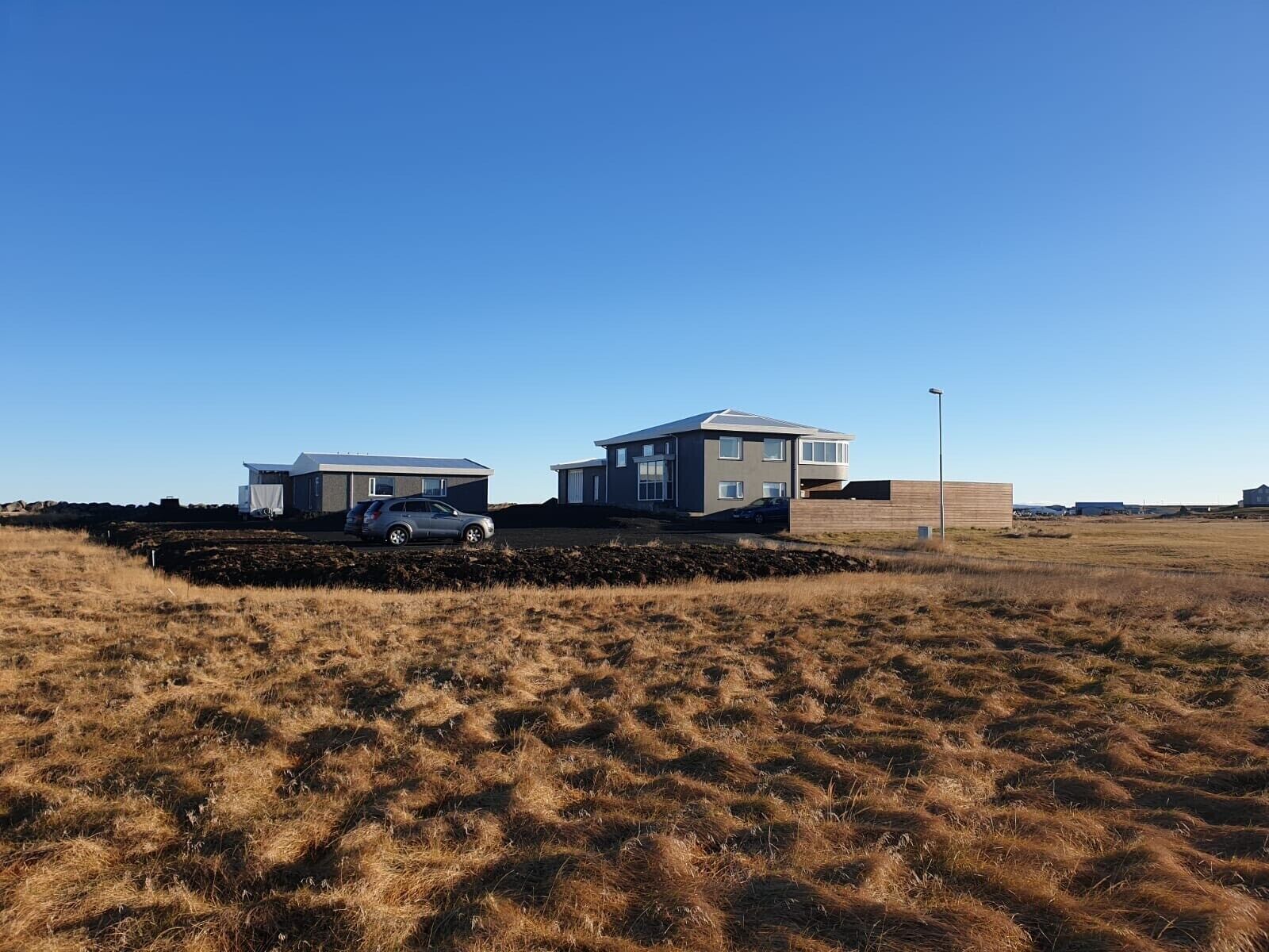 A modern two-story building with a flat roof and large windows, situated in a grassy field with a clear sky.