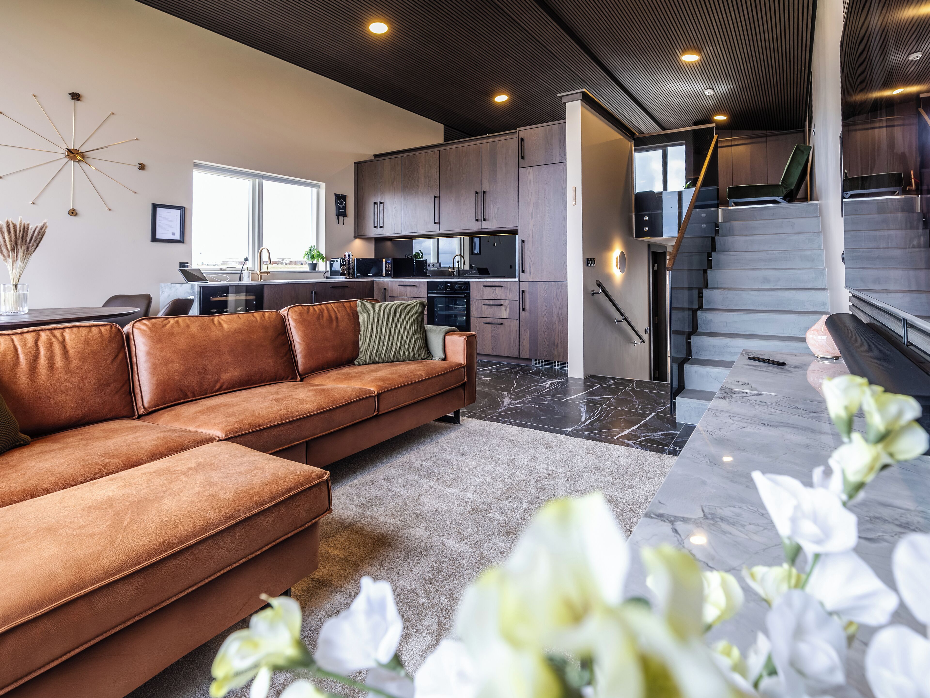 Een modern interieur met een leren bank, keuken, trap en uitzicht op de omgeving.