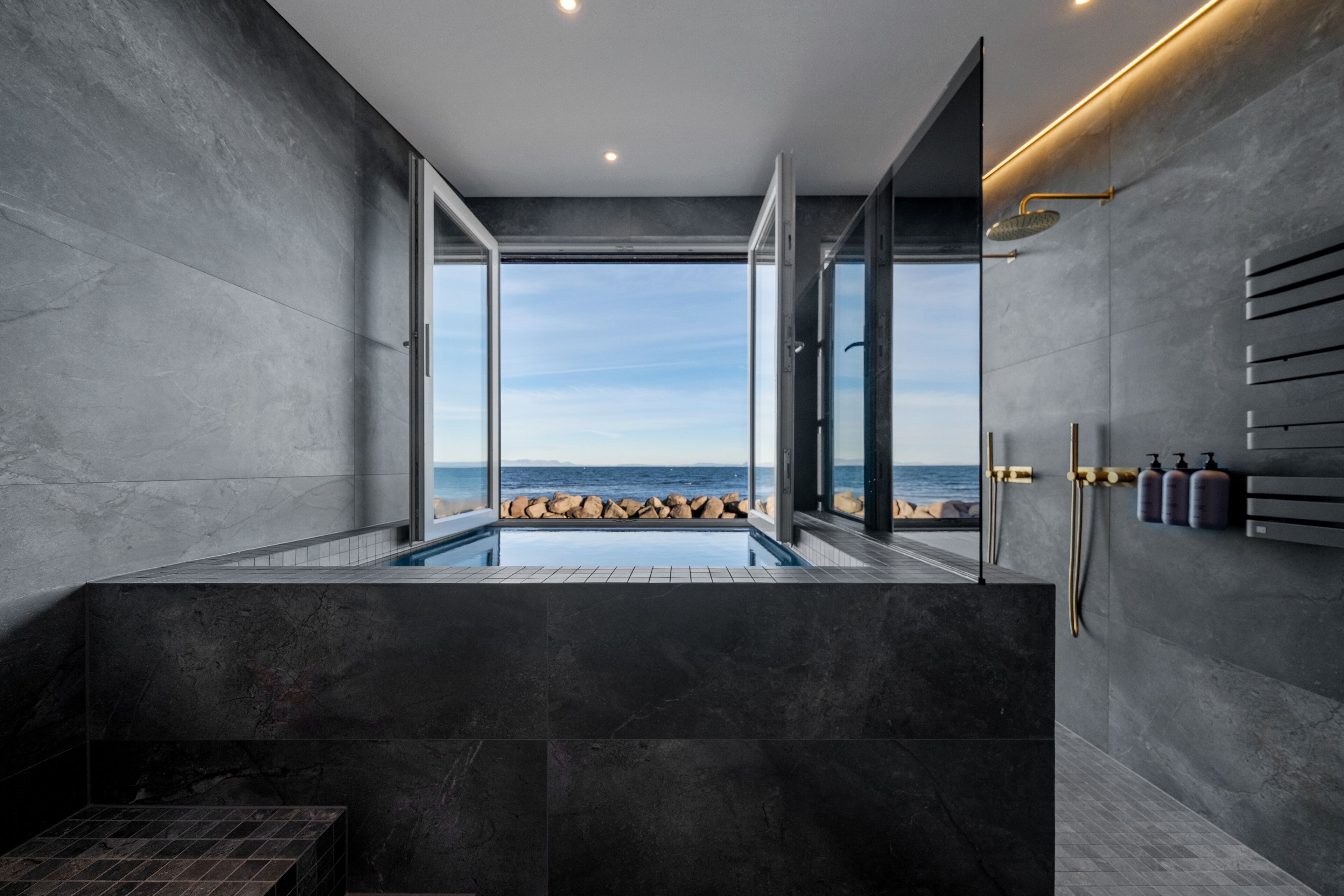 A modern bathroom with a large bathtub, a glass-enclosed shower area, and a view of the ocean.