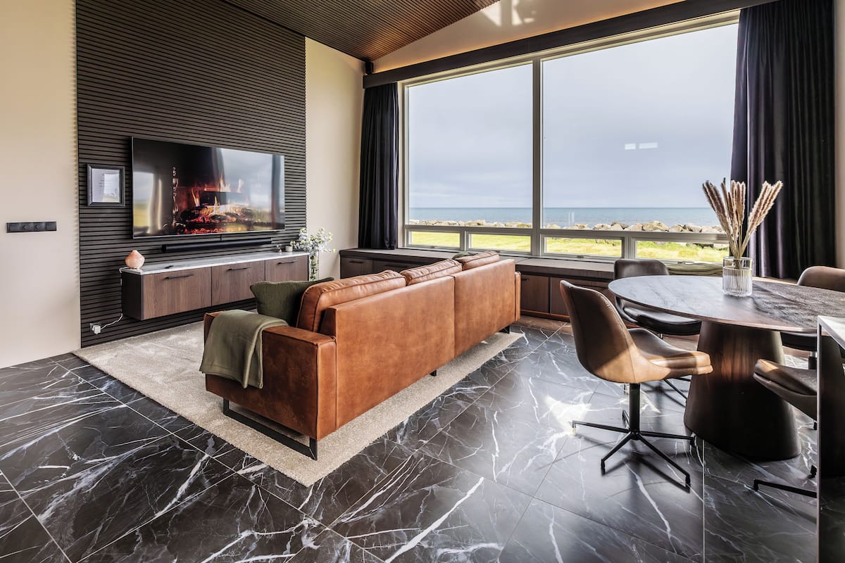Sala moderna com televisão grande, sofá de couro e área de refeições com vista para o mar.