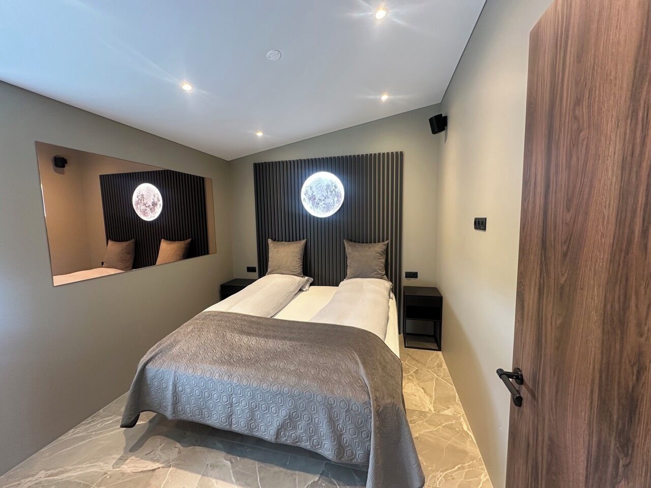 A modern bedroom with a bed, a nightstand, a mirror, and a door.