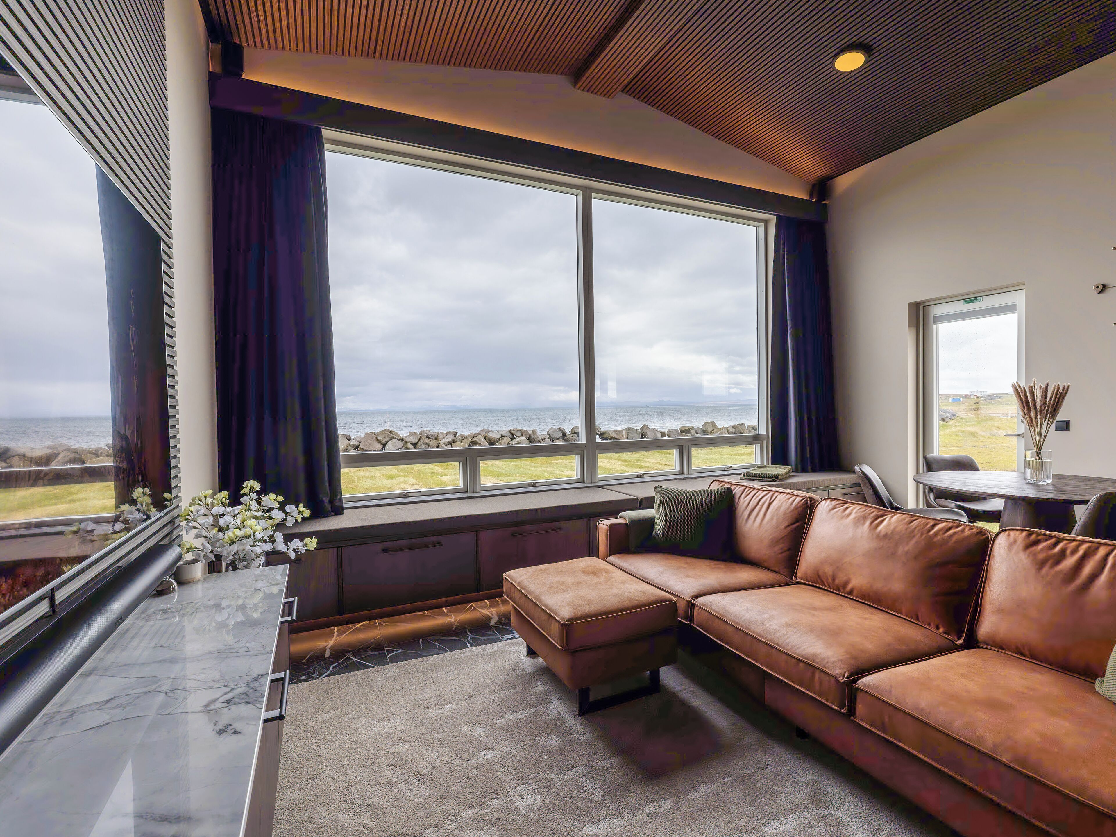 A modern living room with a large window, a brown leather sofa, and a marble floor.