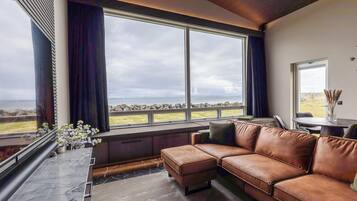 A modern living room with a large window, a brown leather sofa, and a marble floor.