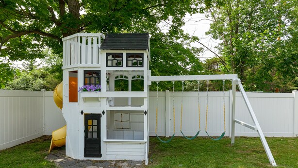 Ein mehrstöckiges Spielhaus mit Rutsche, Schaukeln und einem kleinen Garten.