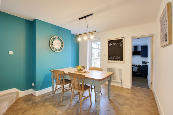 A dining area with a wooden table and chairs, a decorative wall clock, and a chalkboard with writing.