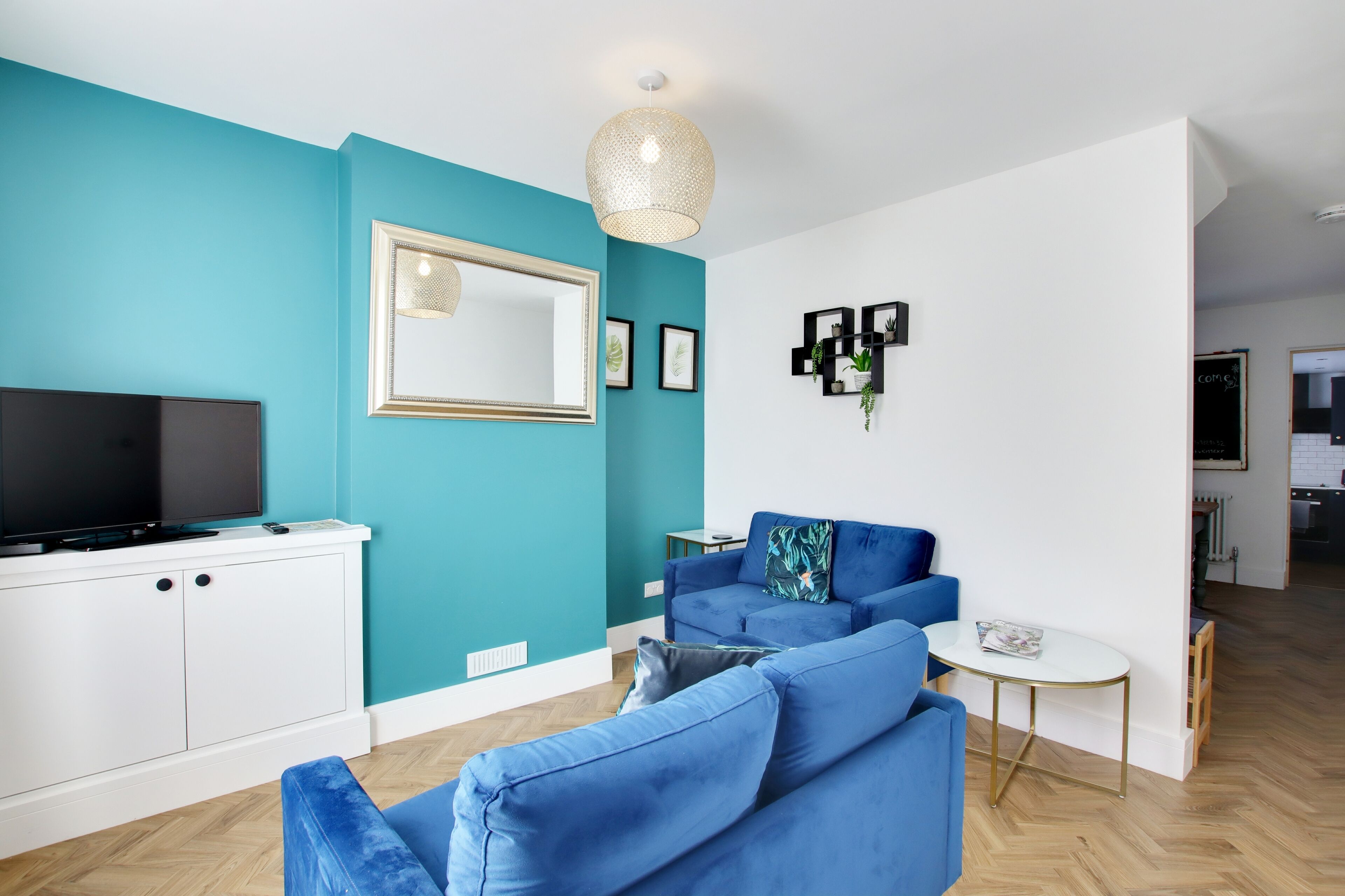 Una sala de estar moderna con paredes color aguamarina, un televisor de pantalla plana grande, un sofá, una mesa de centro y una lámpara colgante.