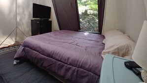 Ein Zeltraum mit Bett, Fernseher auf einem Schrank und einem Fenster mit Blick auf Bäume.