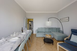 Una sala moderna con un sofá seccional, una mesa de comedor lista para seis personas y una lámpara de pie.