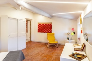 Una habitación con una cama, una silla amarilla, una mesita con una lámpara y un tapiz de pared rojo con estampado.