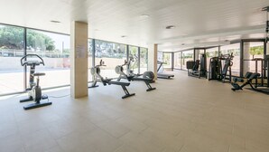 A spacious gym with various exercise equipment, large windows, and a tiled floor. - Apartment SOL CAMBRILS PARK with SPA area (Cambrils)