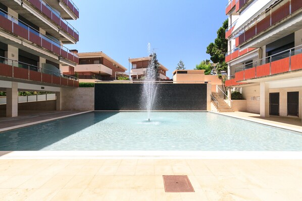 Una piscina con una fuente, rodeada de edificios de varios pisos con balcones.