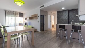 A modern kitchen with a wooden table, bar stools, and a green pendant light. - Apartment SOL CAMBRILS PARK with SPA area (Cambrils)
