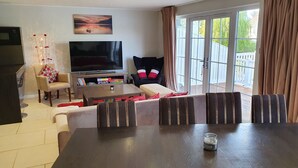 Ett vardagsrum med en platt-TV, ett soffbord, en soffgrupp och ett matbord.